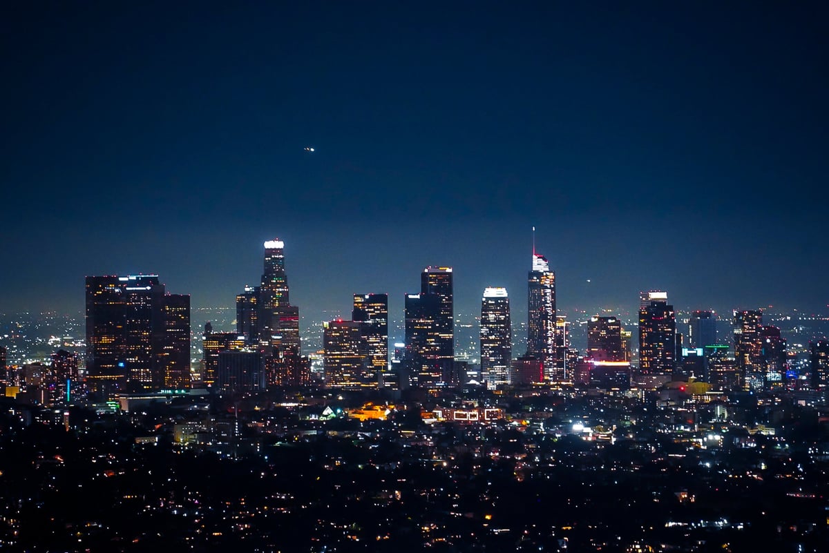 A stunning panoramic view of the Los Angeles skyline at night, captured from a high vantage point. Iconic skyscrapers light up the city, showcasing the vibrant and modern spirit of this Californian metropolis. The image conveys a peaceful nighttime atmosphere while highlighting urban architecture and city energy. No identifiable people are visible, making it suitable for commercial use.